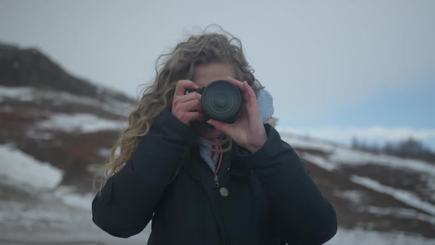 A blonde white woman stands near a mountain during the winter to take photos outdoors
