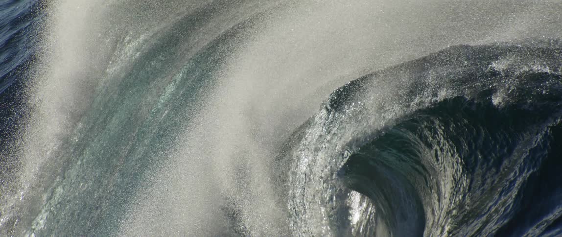 Breaking wave sprays water into the air obscuring its barrel and casting light reflecting water into shadow