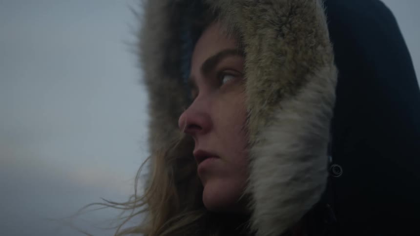 A young white womans hair blows in the wind while shes wearing a coat with a hood outside in the winter
