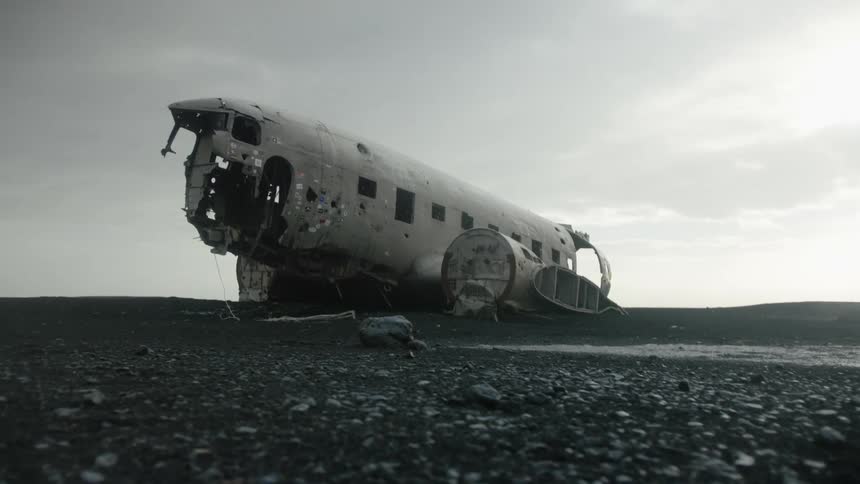 Fuselage of a wrecked plane rests in a desolate landscape under a dark sky