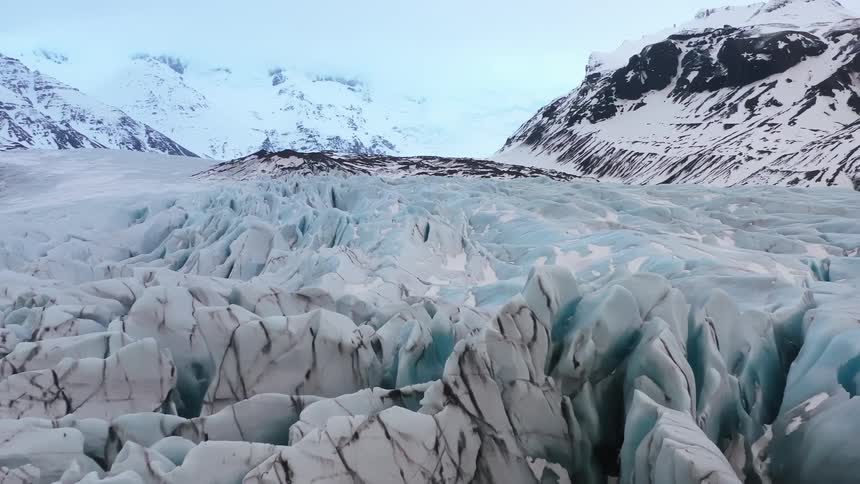 A large glacier melts in a valley surrounded by mountain ranges