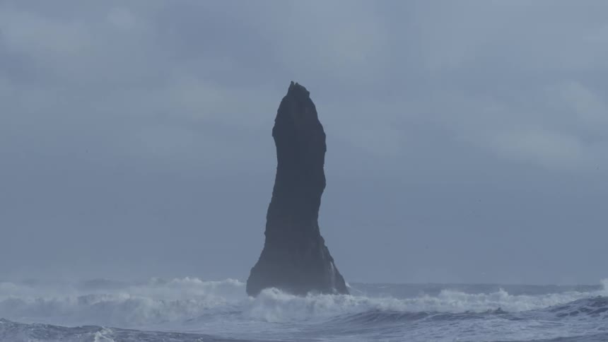 Sharp rock in the middle of the strong sea with foaming waves