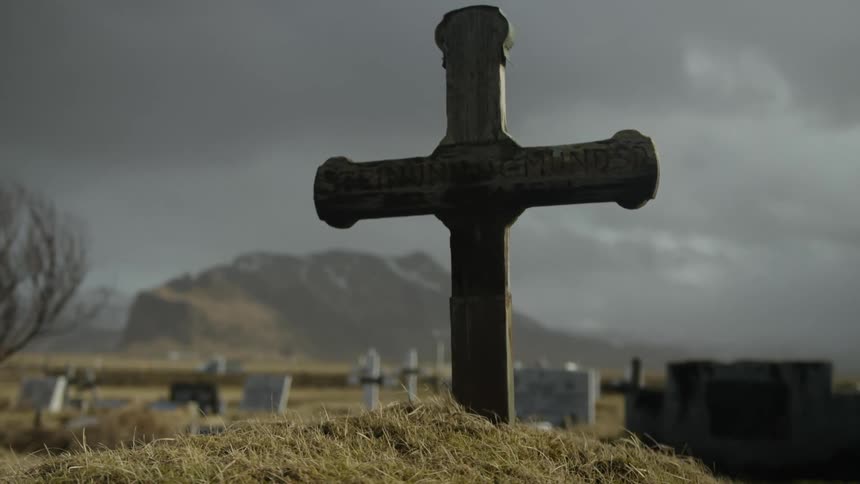 Cross in a cemetery with other tombs in the background in an openair environment