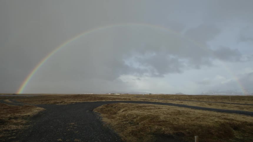 Road forks into two paths under a full rainbow in the sky