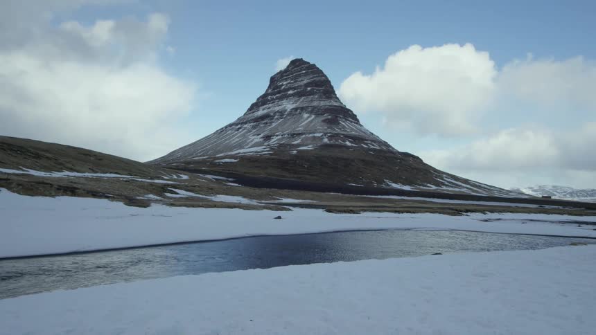 A large pointy mountain juts into the sky near a river and grassy areas