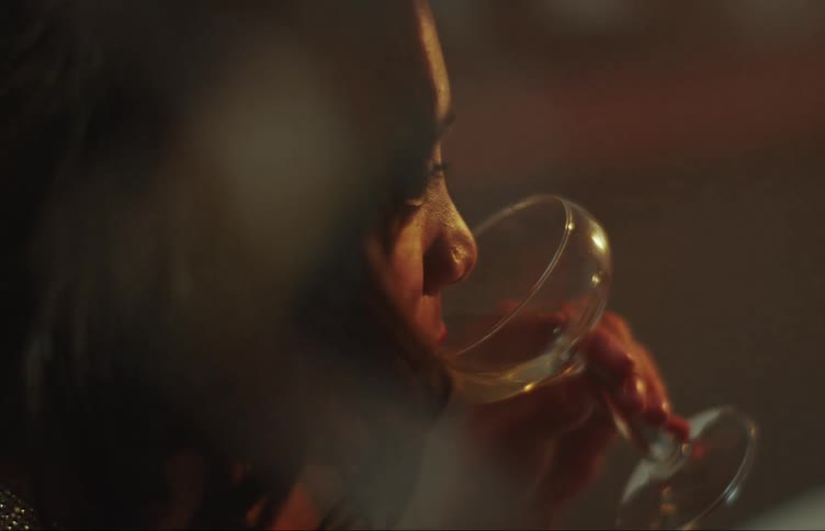 Side portrait of a young woman drinking a cocktail from a crystal glass
