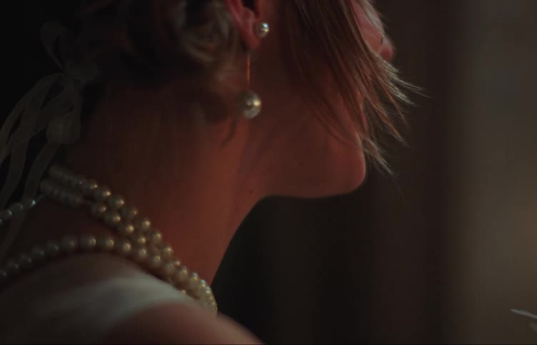 A woman wearing a party dress a pearl necklace and pearl earrings smokes a cigarette