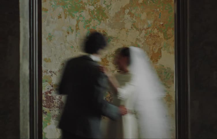 Bride and groom wearing their wedding finery dance in a room with a plastered wall