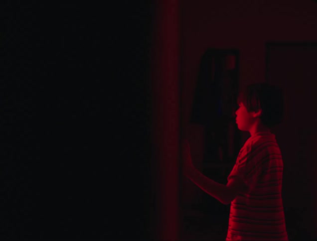 Boy looking into a room that reflects a red light inside a dark house