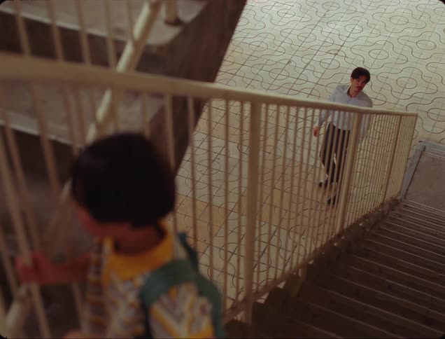 Boy climbing the stairs behind an adult and in the background a man watching and following