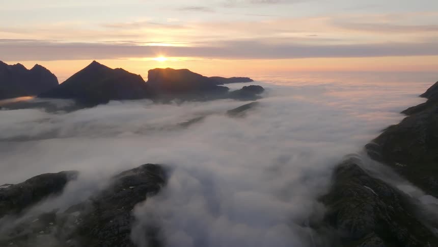 A sunrise over a mountainous landscape with low clouds nestled in the valleys between the peaks