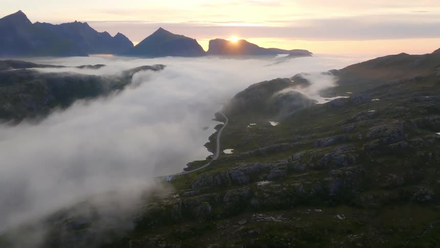 Scenic landscape at dawn with the sun rising between mountain peaks and a blanket of clouds in the valleys