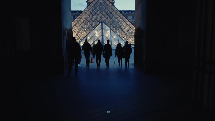 Silhouette of people walking in a corridor and the louvre museum in the background in Paris