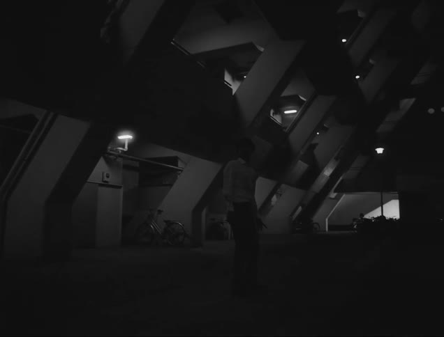A lone person walking through a dimly illuminated tunnel with geometric concrete structures