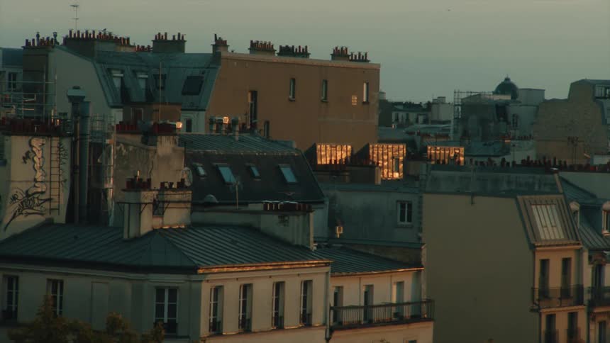 A cityscape during twilight with the warm glow of the setting sun reflecting off windows of an apartment building in Paris