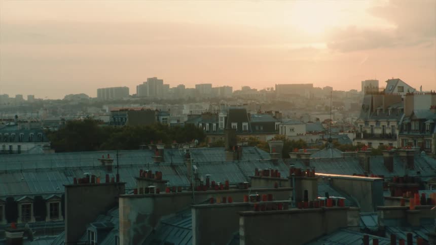 A sunset over a cityscape with buildings in the foreground and a hazy sky in Paris