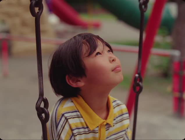 Portrait of a happy boy looking up while sitting on a swing in a park