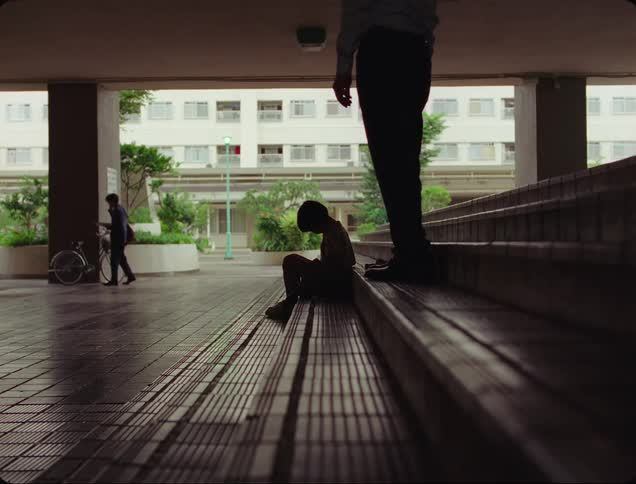 Man approaches and talks to a lone child sitting on the steps in an open air structure