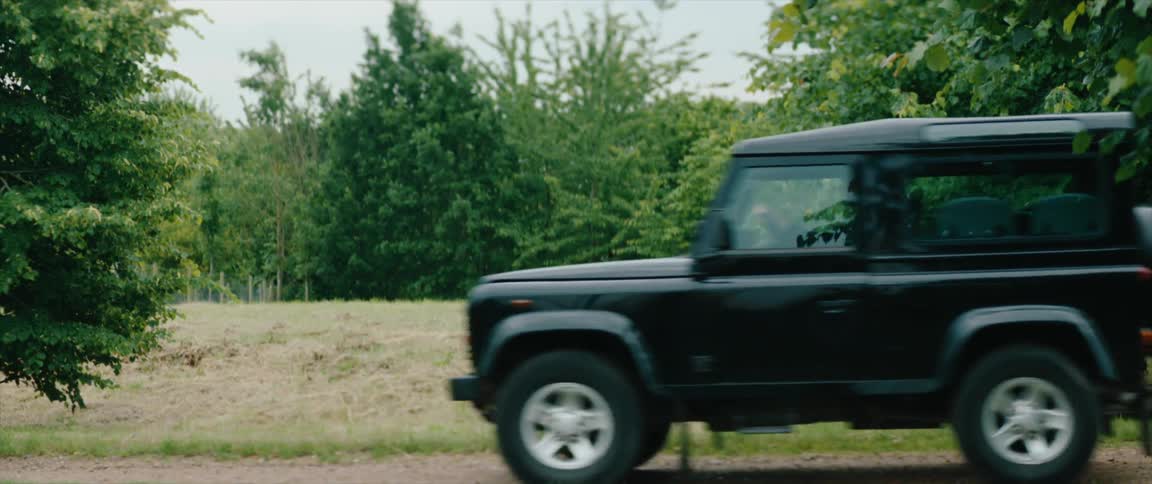 Land Rover Defender passing next to a field with trees