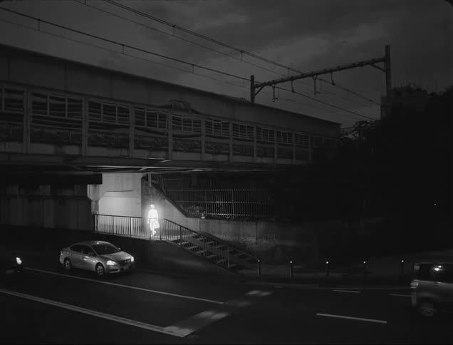 A man glowing with white light walks into a building as heavy traffic passes by on a road