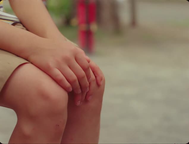 Young person sits outdoors with their hands on their knees