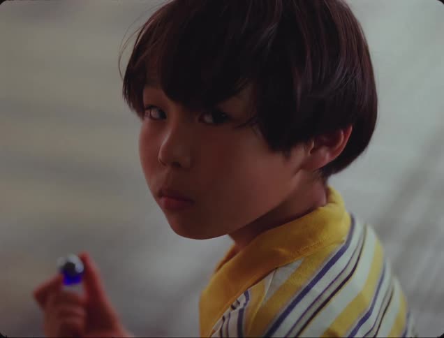 A young boy looks at a blue marble that hes holding before look up and over his shoulder