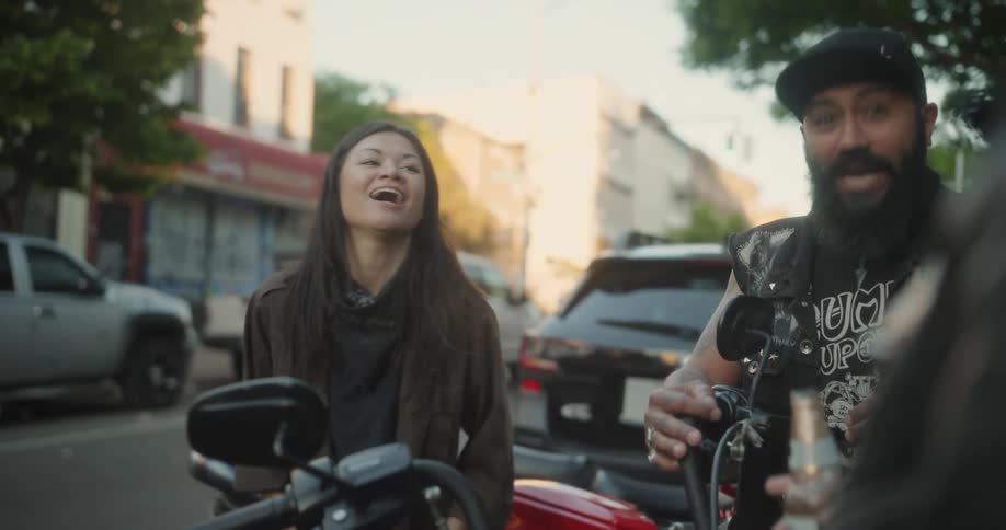 A group of friends standing near a red motorcycle talking and laughing while drinking beer