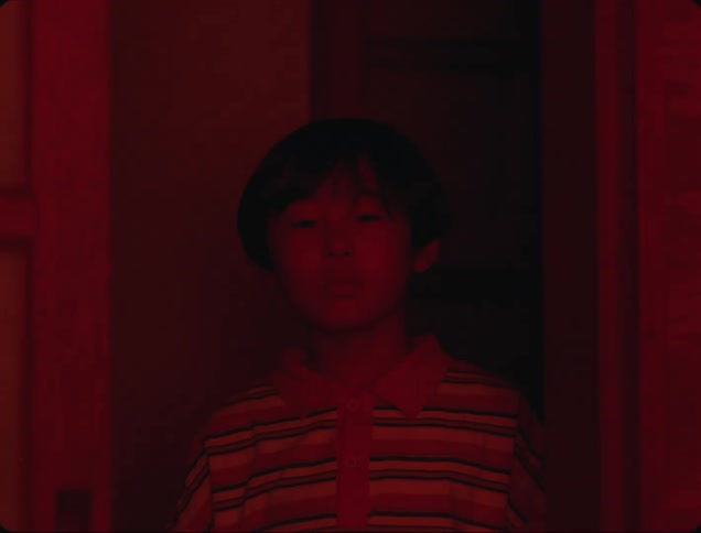 Boy inside the house looking straight ahead and a red light disappears and natural light appears