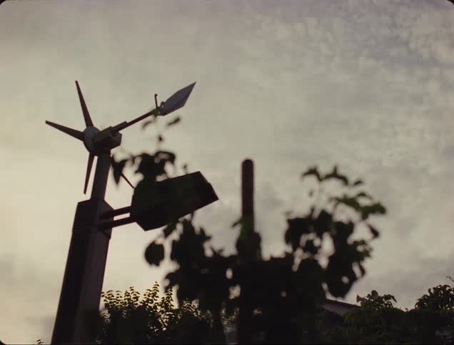 Silhouette of a weather vane against a cloudy sky at dusk