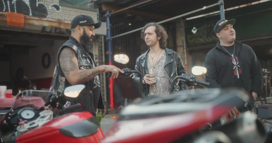 Three friends in a garage with motorcycles talking to each other while drinking beers