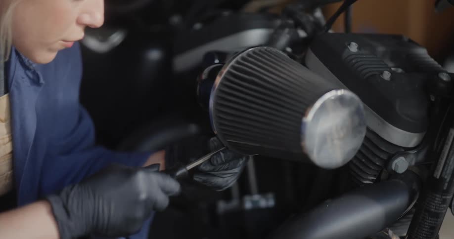 Female mechanic uses a screwdriver to install a part onto a motorcycle