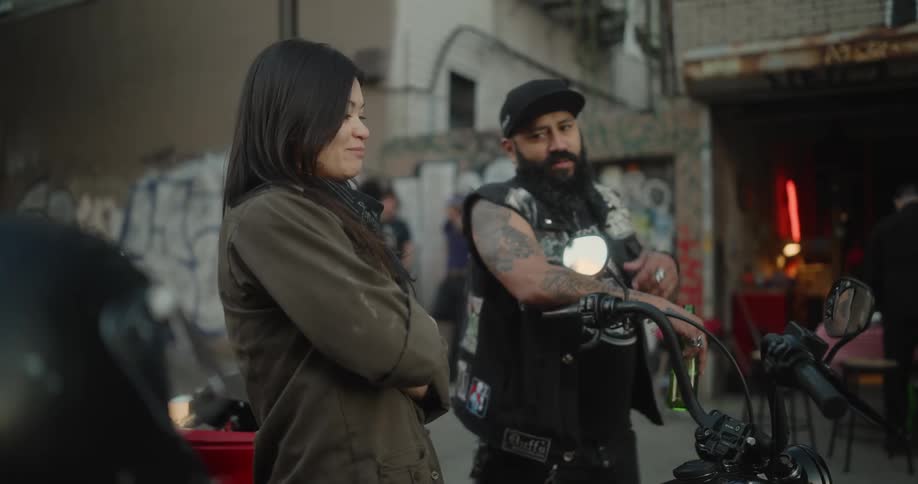 Two friends standing near motorcycles parked in front of a garage in the city talking and laughing