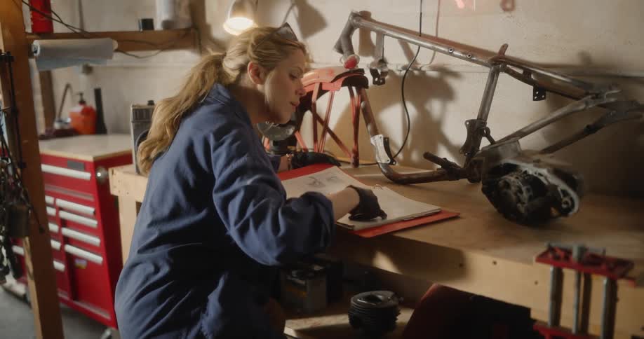 A woman sits at a workbench a reviews information in a binder
