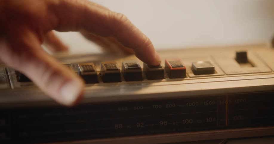 A closeup of a hand pushing a button on an analog radio tuner