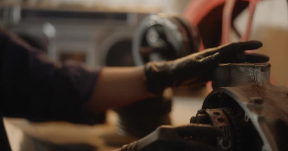 A blonde woman wearing gloves is carefully working on a mechanical part performing maintenance or repairs on machinery