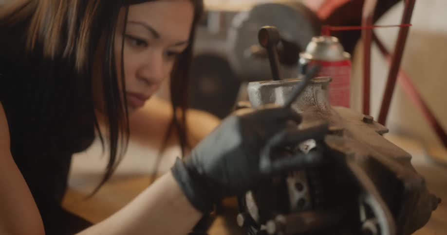 Female mechanic cleans a vehicle part while sitting at a workbench in the garage