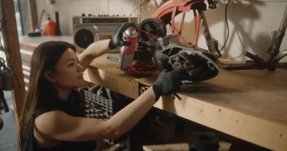 A young woman sprays and fixes a motorcycle part in a garage