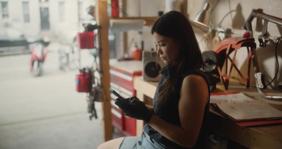 A woman sitting reclined on a workbench texting on her smartphone