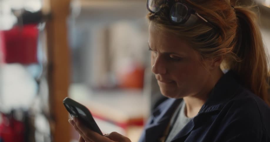 Blonde woman standing in the garage scrolls on her smartphone