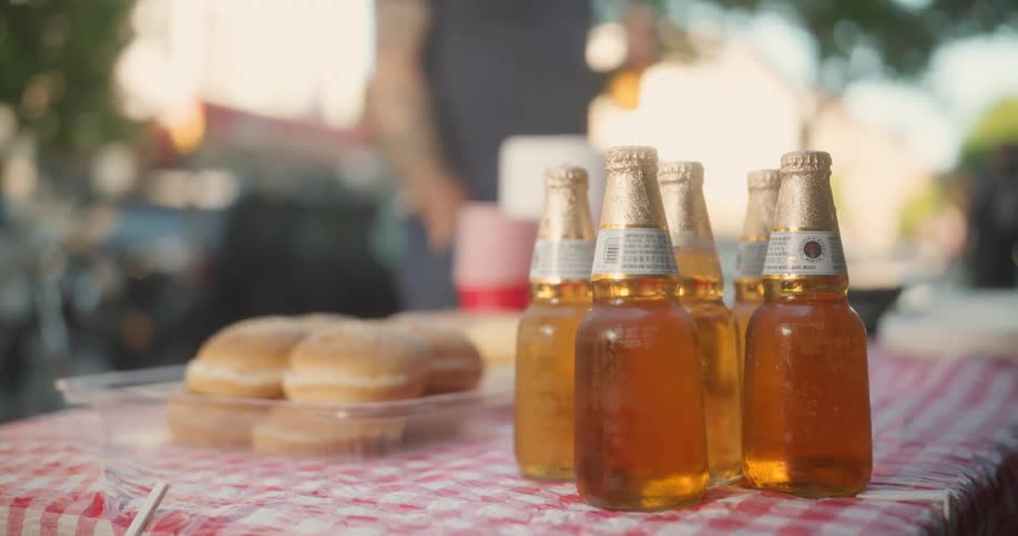 People walk by a man who grabs a beer off of a table outdoors