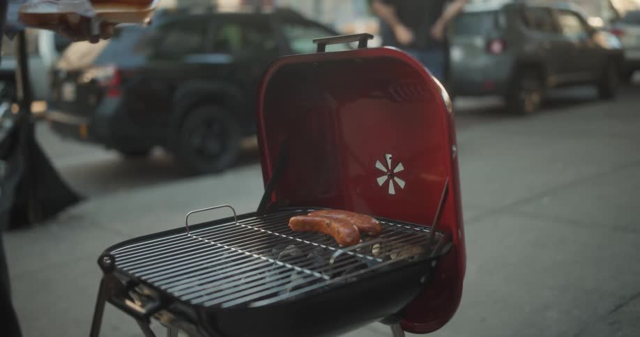 An adult grills hot dogs on a busy sidewalk