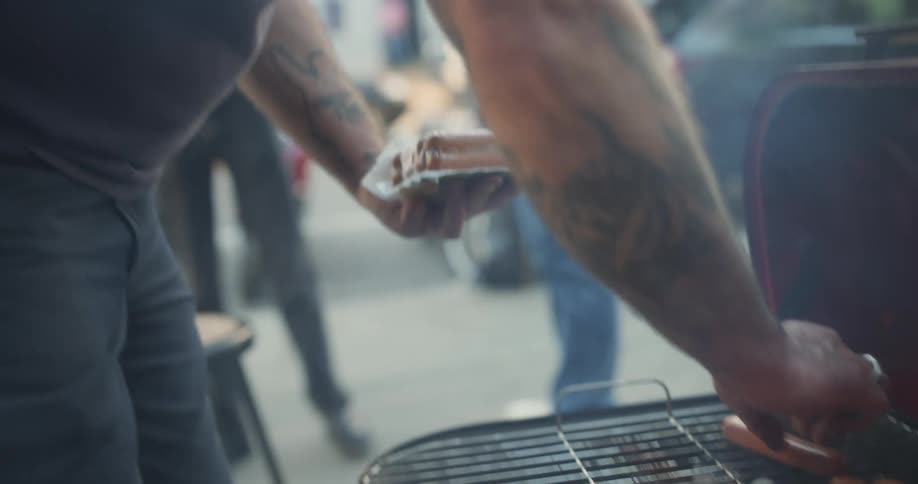 People on the street making hot dogs on a barbecue grill