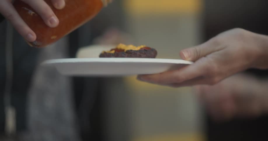 People putting sauces on a burger on a plate