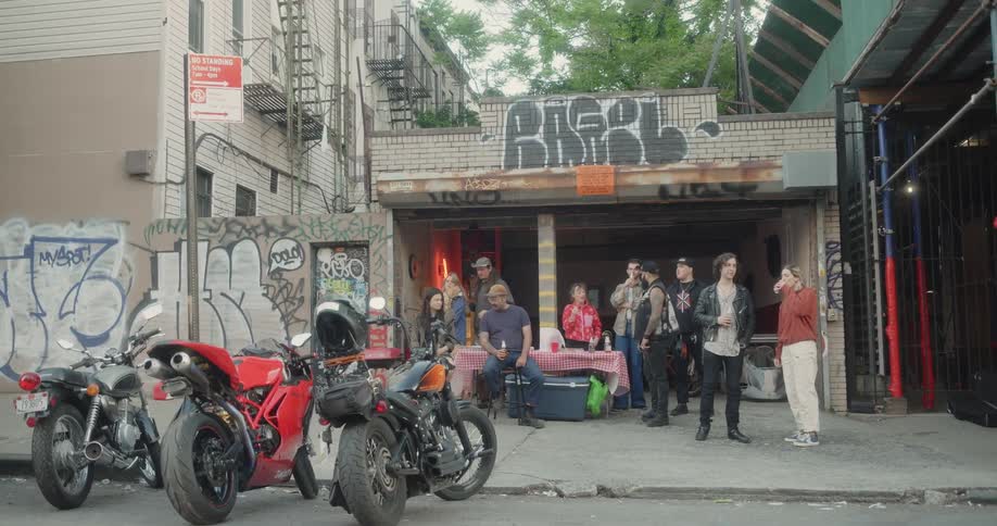A group of people meet up and talk and drink on the sidewalk next to a road