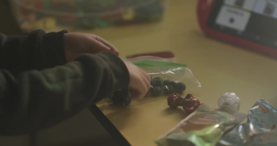 A child hands sort through various colorful fruits and sweets on a yellow surface