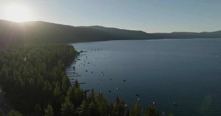 Aerial panorama of a lake surrounded by mountains and vegetation with the sun setting on the horizon