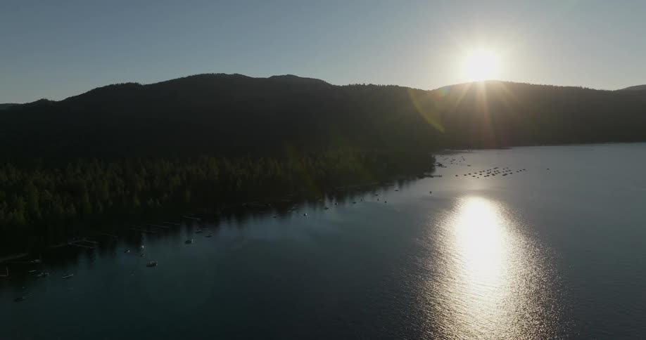 The sun is set just above the top of a mountain range near a large body of water