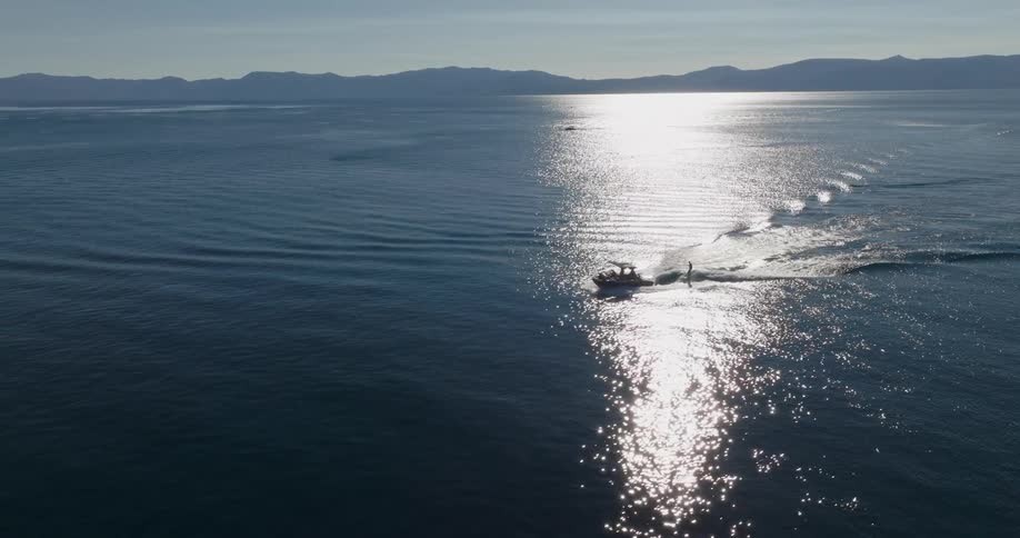 Aerial view of a boat isolated by the moving sea and with a person behind a board anchored to a rope on the boat
