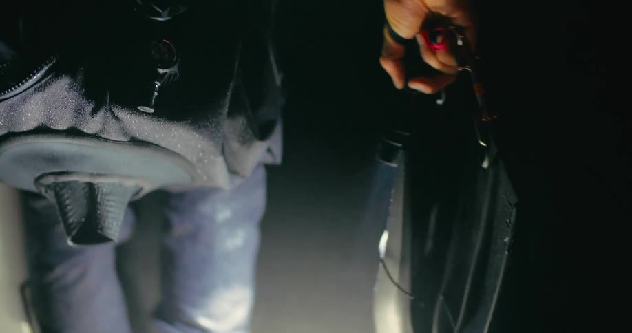 A person is walking in a dark place carrying a bag and there is lighting with a flashlight that is in his hand