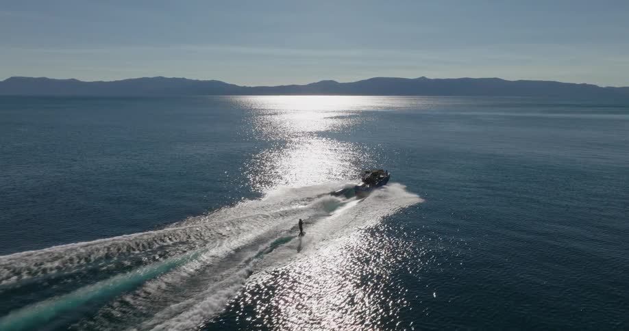 People surfing behind a boat with a rope attached in a calm sea with mountains on the horizon
